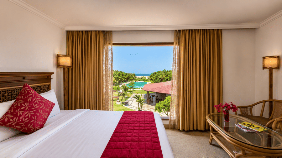 Ocean View Room with a king bed, red accents, and a balcony overlooking the pool and greenery at Chariot Beach Resorts, offering a scenic stay