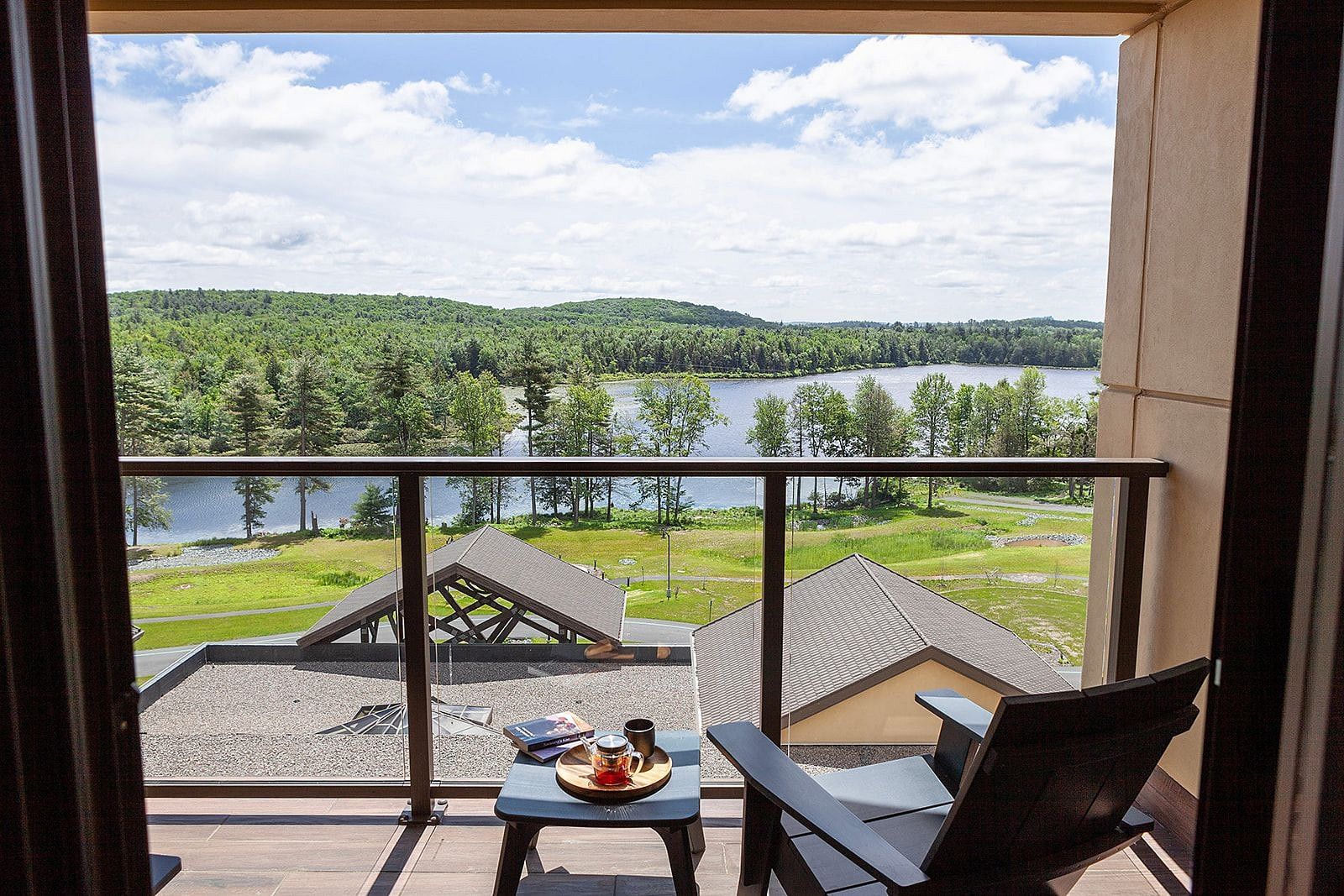 A balcony view overlooking a serene lake and lush green trees and a lake, with a chair and small table holding refreshments at YO1 Longevity and Health Resort.