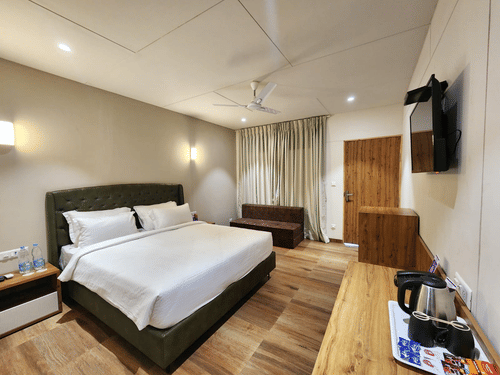 The interior view of a cottage in Daman featuring ceiling fan, a double bed, wall mounted bed lights, and a TV | VITS Daman Devka Beach