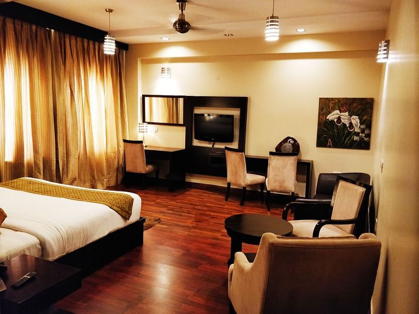 A room consisting of a clean bed, sofa chairs, a coffee table, a TV and wall paintings - Five Elements Hotels