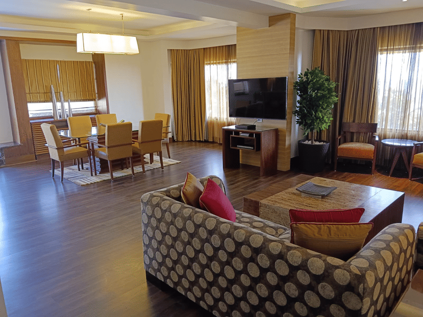 Spacious suite living and dining area at Retreat with patterned sofa wooden flooring a wall-mounted TV and a dining table with yellow chairs in a warmly lit open layout.