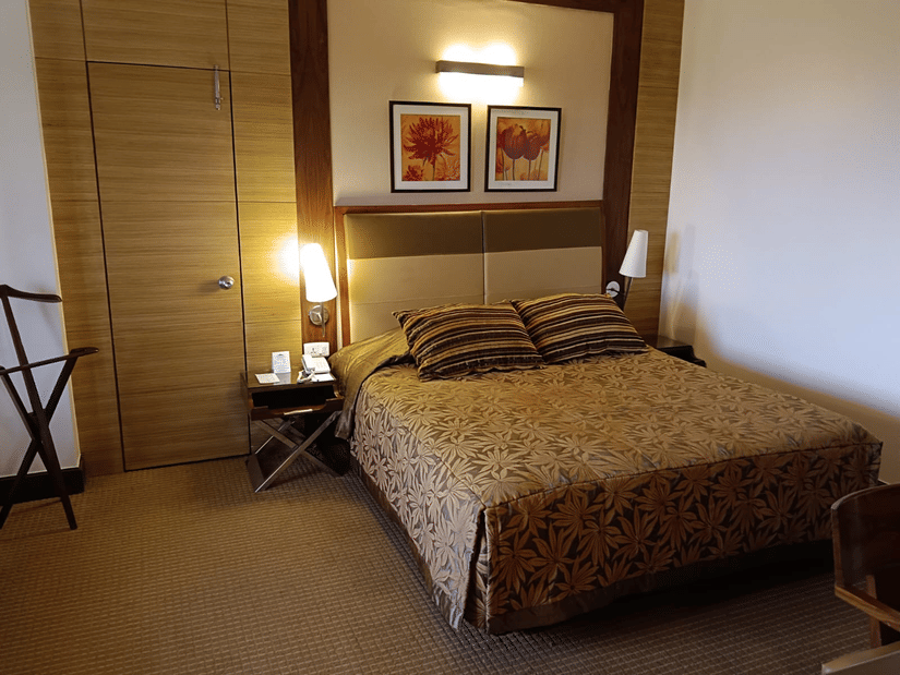 A bedroom featuring a patterned bedspread, coordinating pillows, framed floral artwork above the headboard, and a door on the left side - The Retreat Hotel and Convention Centre