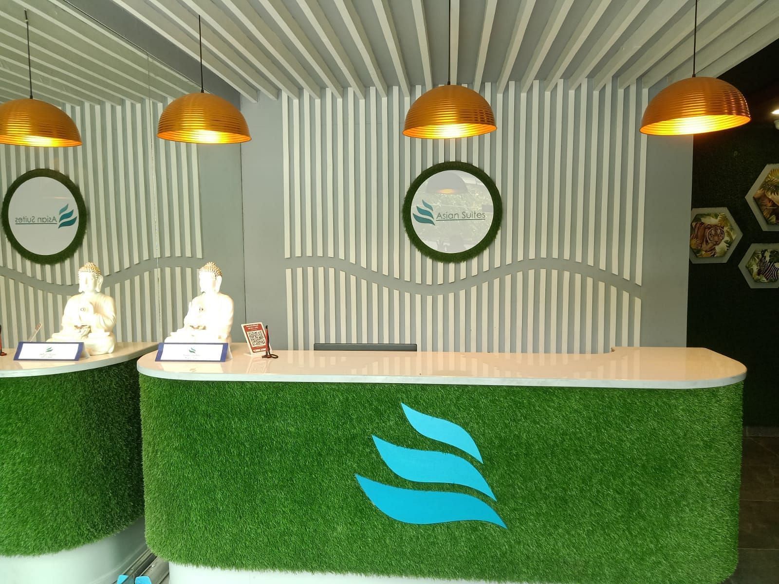 A vibrant green reception desk with staff members standing behind it, under pendant lights - Asian Suites IFFCO Metro, Gurgaon