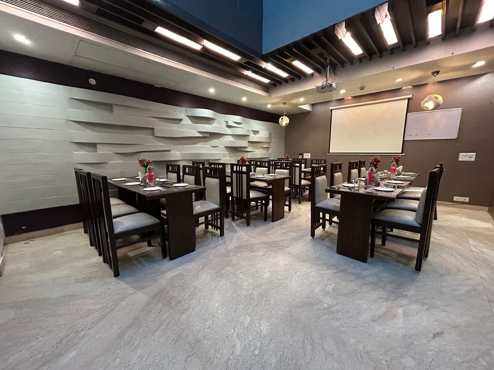 A modern dining space with neatly arranged tables and chairs, set against sleek grey walls with stylish ceiling lights - Hotel Emerald, Chandigarh