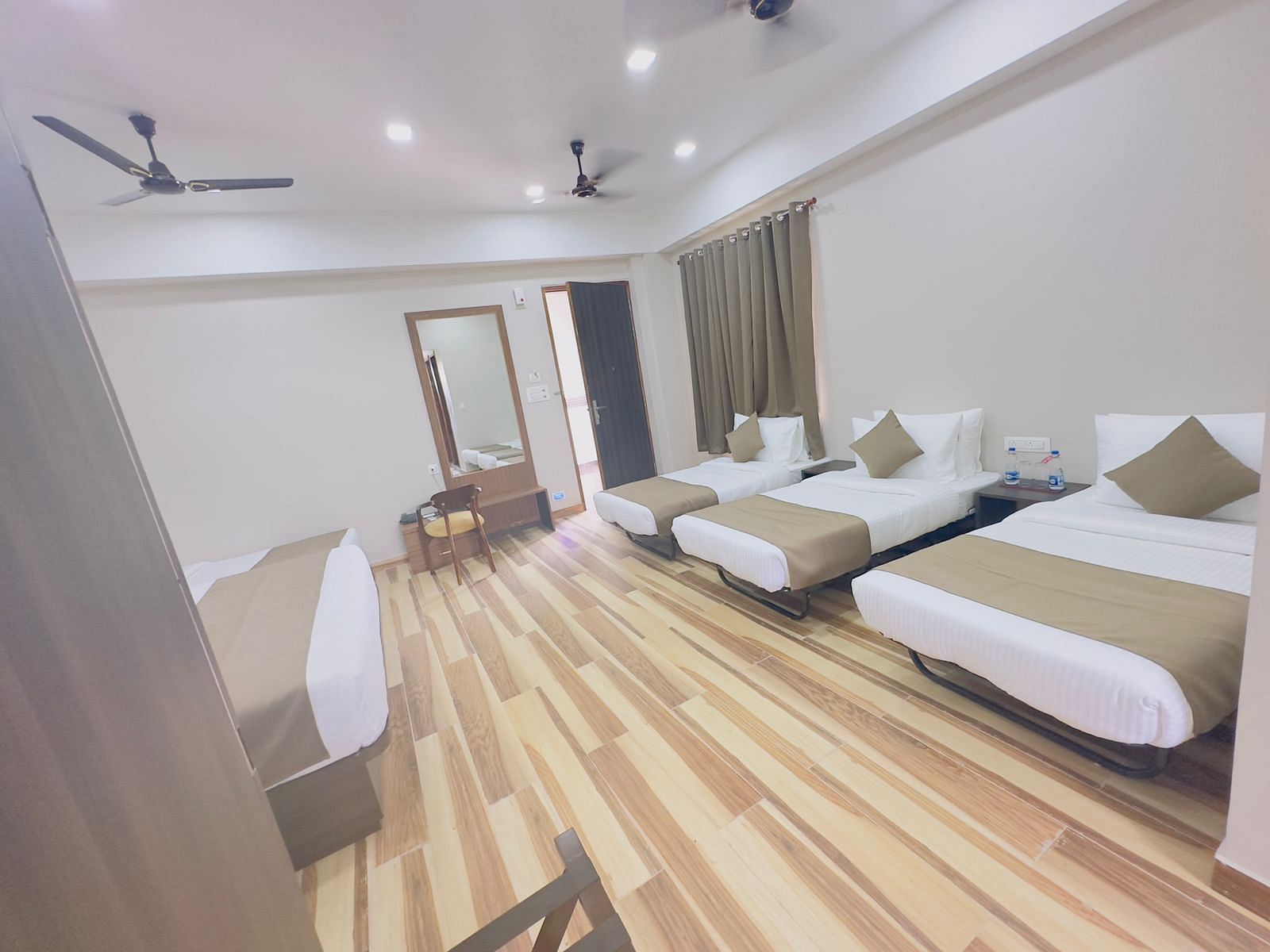 A spacious room features double beds with white and beige bedding, wooden floors, and ceiling fans - Kankidham Lords Inn