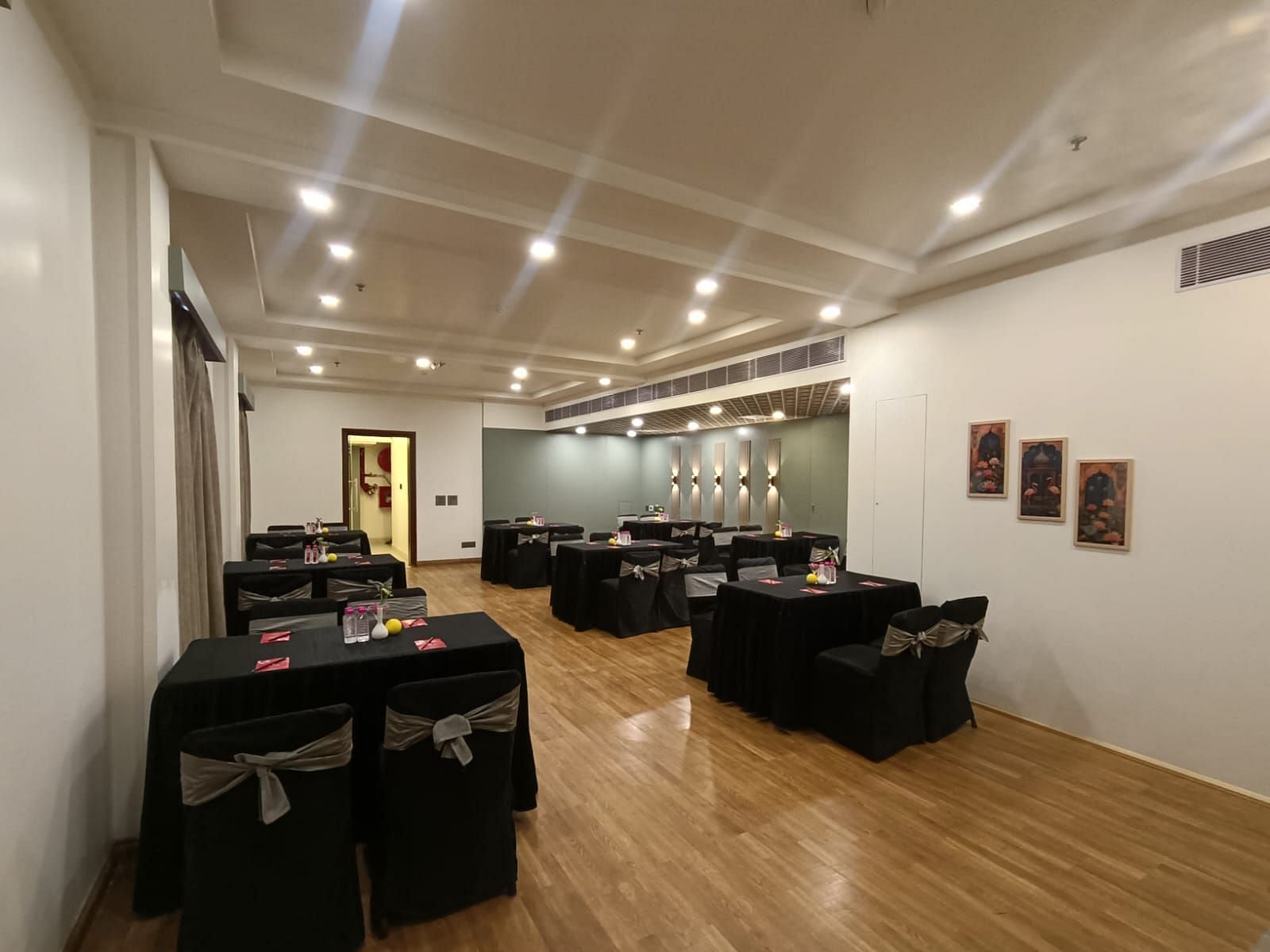 Conference room with rectangular tables covered with black satin covers and chairs under white ceiling lights at Lords Plaza Jaipur.