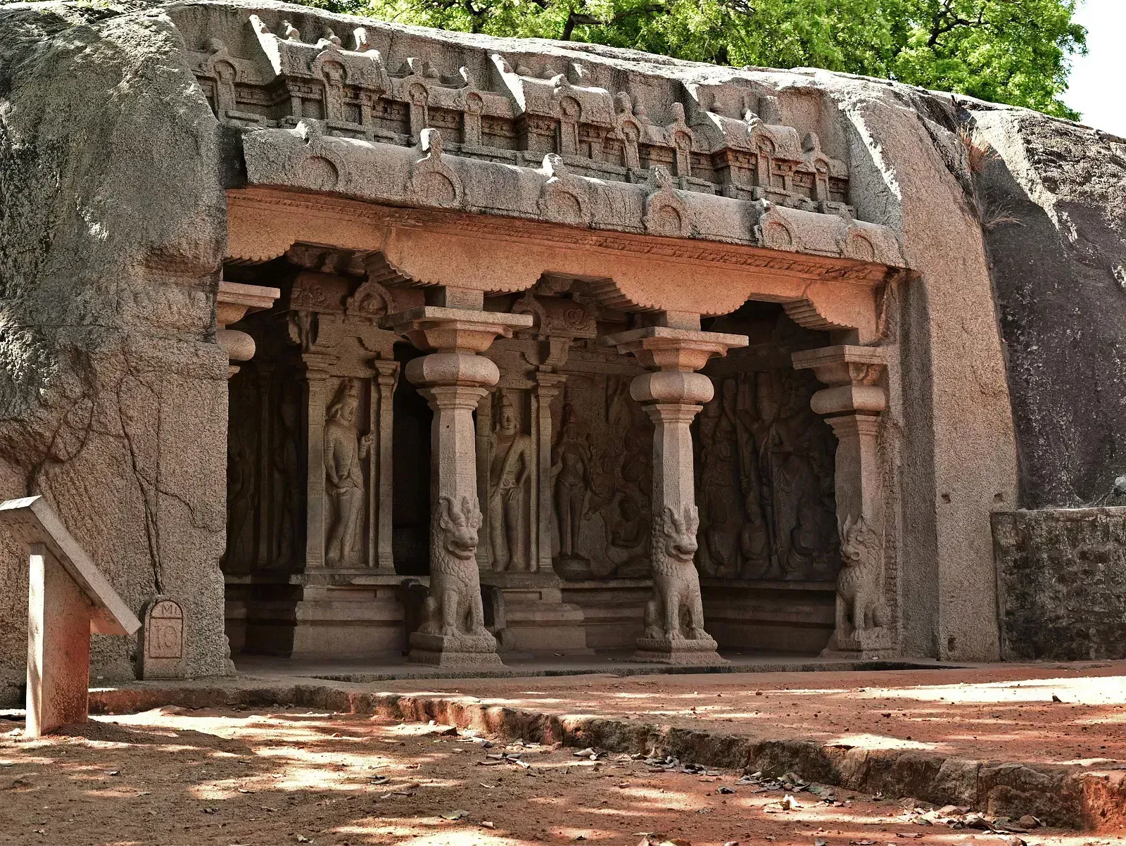 A rock-cut temple facade with sculpted pillars and a detailed entrance, bathed in natural light.