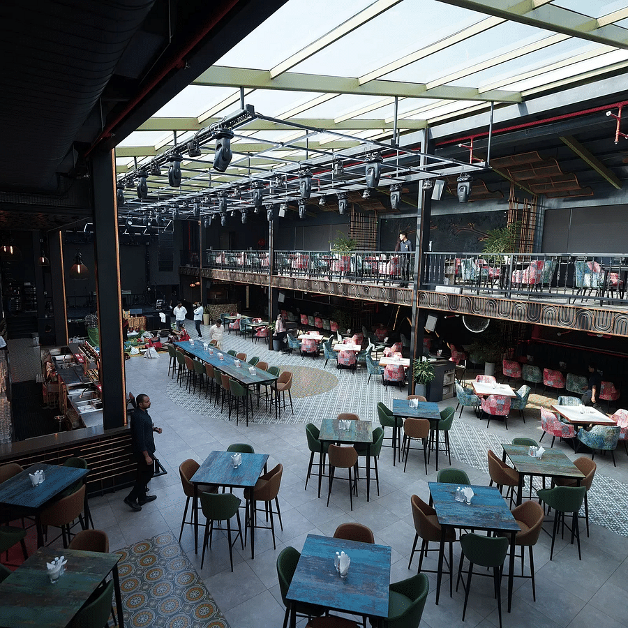 alt-text Interior view of a spacious restaurant with a glass ceiling, featuring a mix of seating arrangements, tables, and a vibrant decor, and staff members attending to guests - Clarion Bangalore