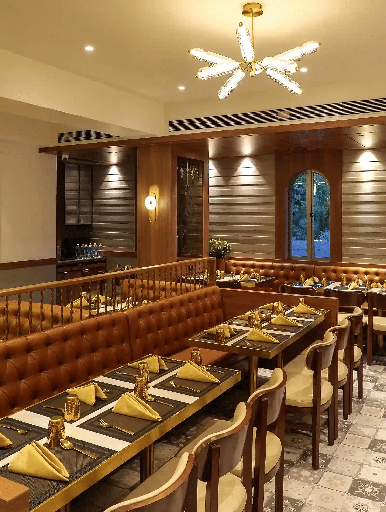 Neatly arranged seating tables with modern lighting and a double-door window and a CCTV at Naivedya Restaurant in Melior Inn, Mumbai.