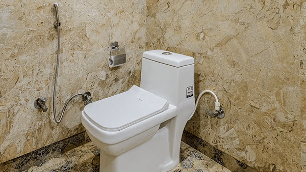 A bathroom with a toilet and jet spray fittings, featuring beige tiled walls - Lime Tree Hotel Vrindavan
