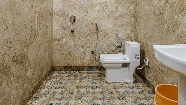 A spacious bathroom with one toilet and a washbasin, set against beige marble tiles - Lime Tree Hotel Vrindavan