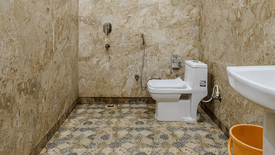 A spacious bathroom with one toilet and a washbasin, set against beige marble tiles - Lime Tree Hotel Vrindavan