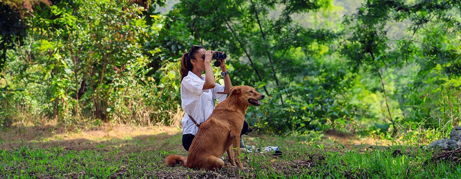 A dog sitting next to a woman watching through binoculars at The Sylvan Retreat, Dehradun.