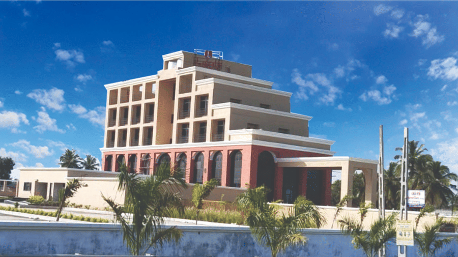 Multi-storey modern hotel building exterior of Lords Swastik Studio, Kodinar, surrounded by plants under a bright sky.