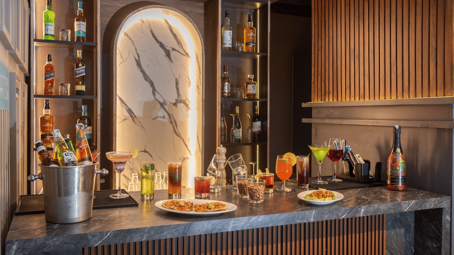 A bar counter featuring various bottles, glasses, a cocktail shaker, and small plates of food | Lawrence Solitaire Resort, Nainital