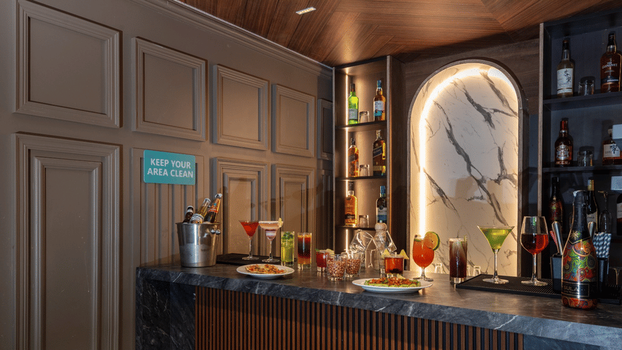 A marble-topped bar counter with various cocktails, bottles, and a snack plate in front of a wooden panelled wall | Lawrence Solitaire Resort, Nainital