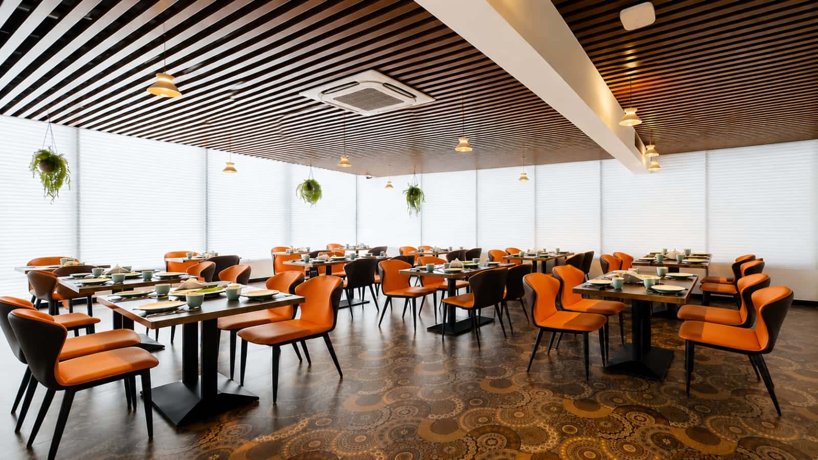 The restaurant at Hotel Ritvi's Elite laid for service, orange and black chairs at dark tables under a slatted timber ceiling