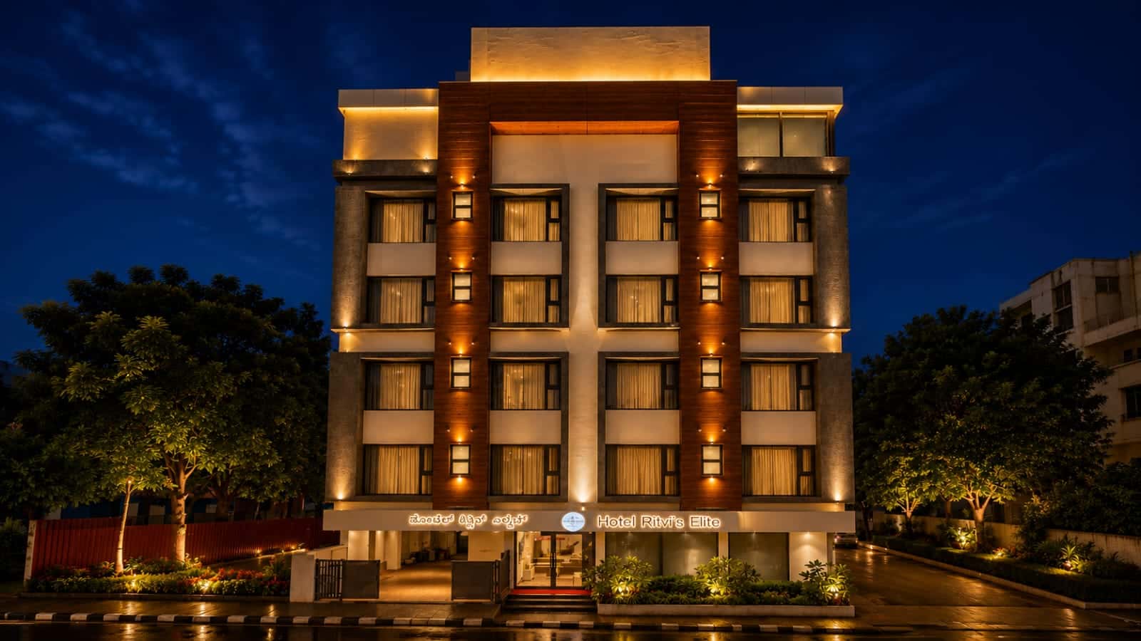Hotel Ritvi's Elite lit up after dark, warm light in every window and the entrance signage glowing beneath a deep blue sky