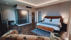 An image of a bedroom with king size bed, ceilng lights, bedside table and lamp, a small table at one corner and a chair next to it -  Hotel Polo Towers, Agartala