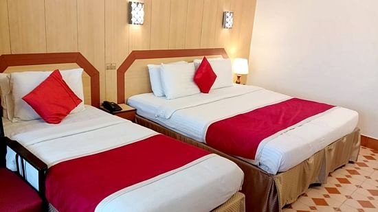 Room with a single bed, a double bed, bedside lamp, and wall-mounted lights at Hotel Swagath, Bangalore