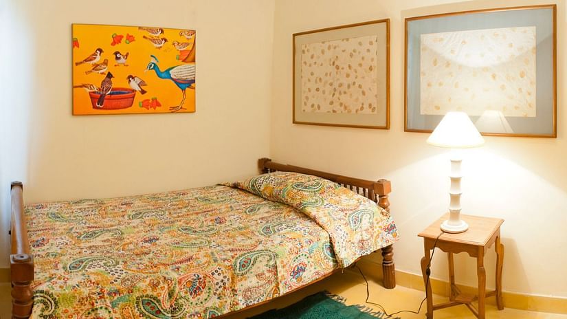 A guest room at Tijara Fort-Palace - 19th Century, Alwar features a single bed with a patterned cover, a bedside table with a lamp, and artwork on the wall.