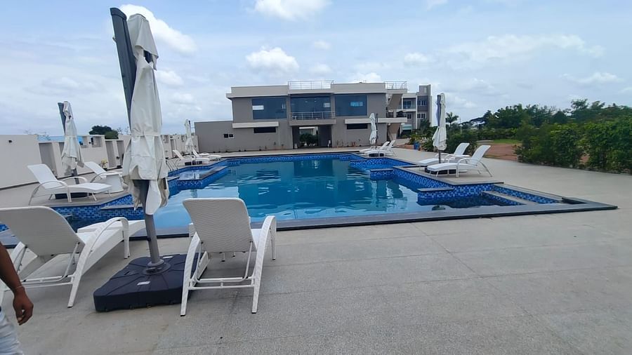 Rooftop swimming pool with tiled edges, surrounded by lounge chairs and closed umbrellas; a modern building is visible in the background, with trees and open space to the right. A person is partially visible in the foreground on the left - Kyriad Prestige,
