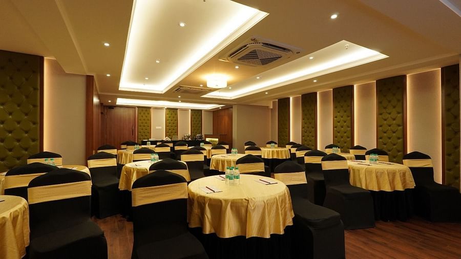 Spacious conference hall with U-shaped wooden table, cushioned black chairs, projector, white screen, and recessed ceiling lights – Magnus Nexstar Suites, Kalyani Nagar
