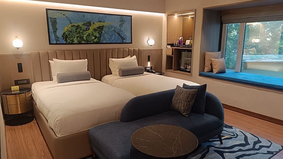 Twin room with two single beds, a blue sofa, window seating, modern lighting, and a minibar with refreshments - Pride Hotel Pune