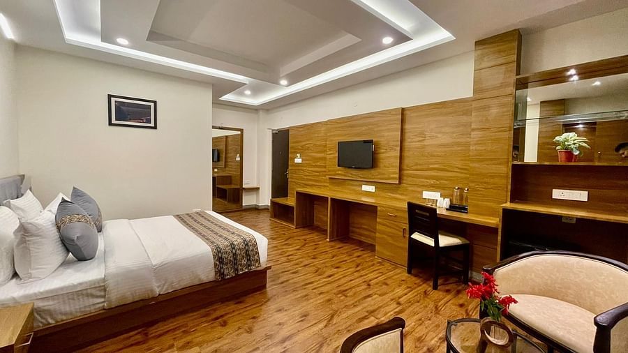 A room that has a bed, TV on the wall, wooden desks, two chairs, and a teapoy | Voyage The Royal Retreat, Gangtok