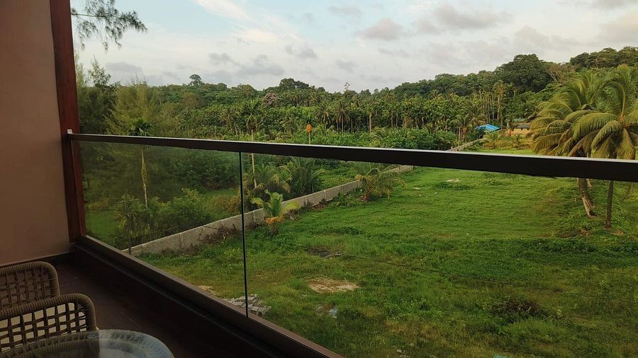 A serene view from a balcony of Superior Forest View Room at Silver Sand Sea Princess Beach Resort, Port Blair, showing a lush green lawn and dense trees under a cloudy sky.