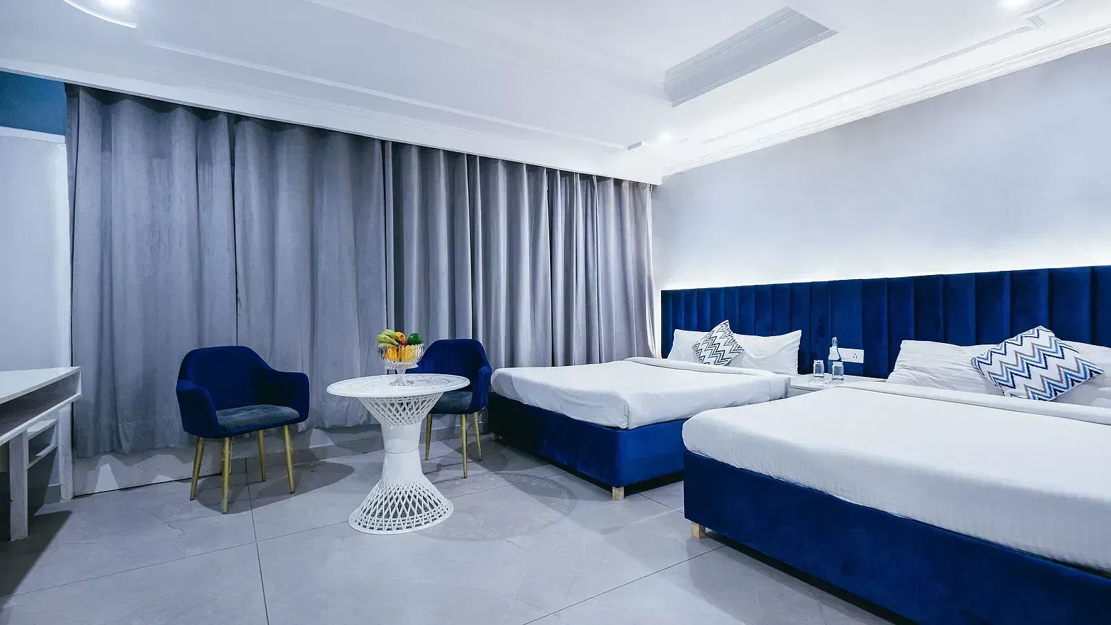 Family Room featuring two king beds with white linens and blue accents, along with sheer white curtains. - Hotel Downtown17, Chandigarh