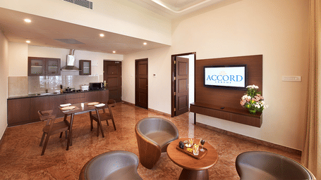 A wide angle shot of a living area in Studio Two Bedroom Suite featuring cosy seating arrangement, a wall mounted television and a kitchenette at Accord Chrome Airport Hotel