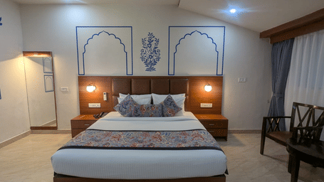 A Family Room with a neatly made bed featuring colourful floral pillows and a matching bed runner. The wall art includes blue arch designs and a floral motif, adding a touch of elegance. Warm lighting and neutral tones create a relaxing ambience at  Bamboo