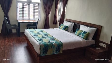 A double bed with chairs & study table next to it inside Premium room with balcony - Ecotel Kolkata