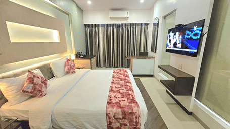 Deluxe Room at Hotel Mumbai House, Thane, featuring a king bed with pink patterned linen, modern wall lighting, and a TV.
