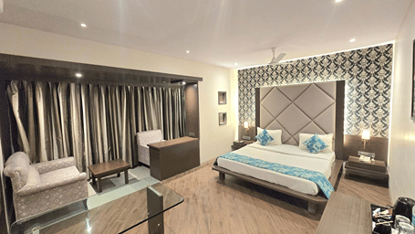 Luxury Room at Hotel Mumbai House, Thane, displaying a king bed set against a decorative wallpaper headboard, sofa, and floor-to-ceiling drapes.