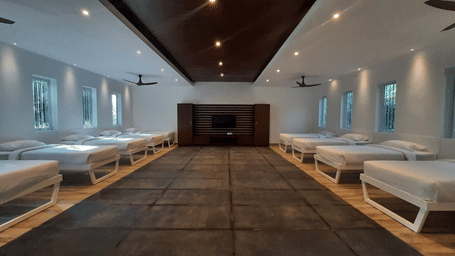 Club room at RD's Nature Retreat in Bangalore featuring multiple bed placed on either side of a huge room and at the end of the room there is a flat TV screen on the wall.
