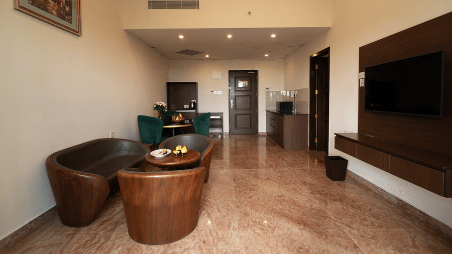 A living area in Studio Two Bedroom Suite in Chennai with a cosy seating arrangement placed in front of a wall-mounted television at Accord Chrome Airport Hotel