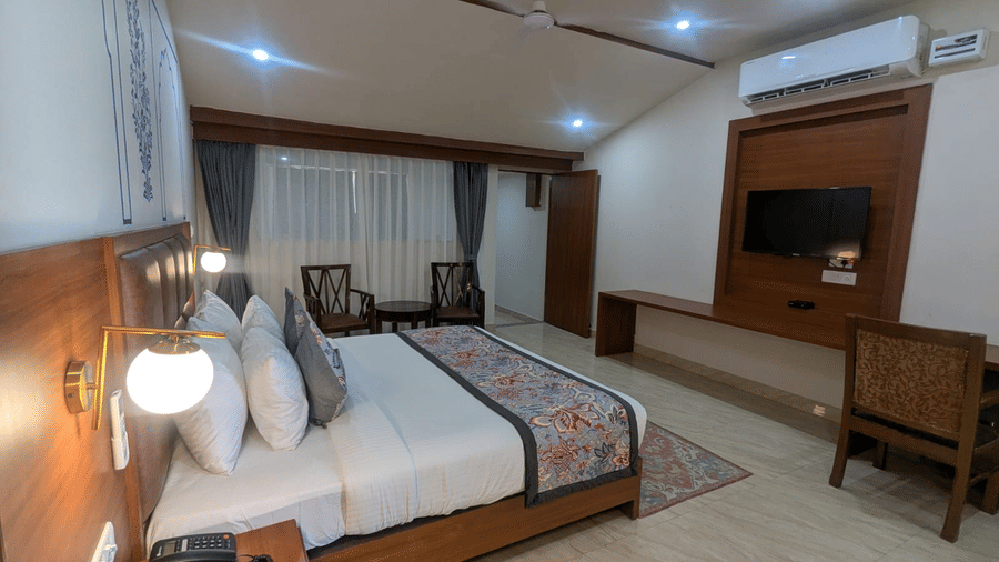 A Family Room with a neatly made bed, decorative pillows, and wall art. A desk beneath a wall-mounted TV adds functionality. Bright, calming ambiance at  Bamboo Saa Sunrrise Wedding & Wellness Resort, Jaipur.