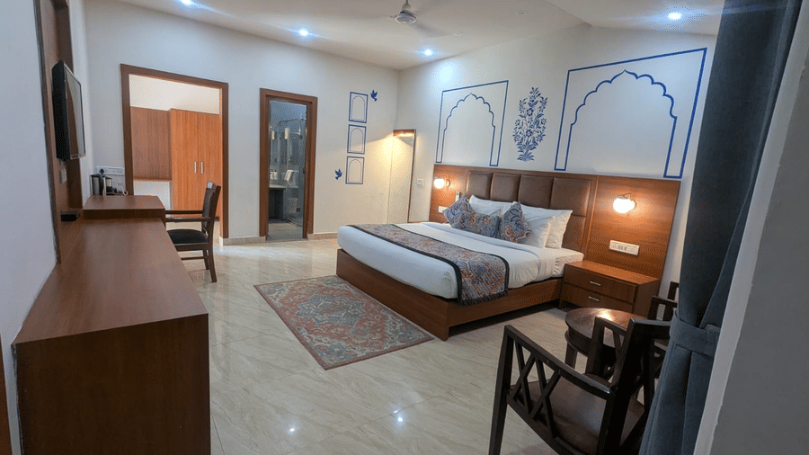 A Family Room  with a large bed, adorned with patterned pillows and a rug. Elegant wall art, wooden furniture, and warm lighting create a cosy ambience  at  Bamboo Saa Sunrrise Wedding & Wellness Resort, Jaipur.