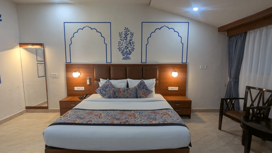 A Family Room with a neatly made bed featuring colourful floral pillows and a matching bed runner. The wall art includes blue arch designs and a floral motif, adding a touch of elegance. Warm lighting and neutral tones create a relaxing ambience at  Bamboo