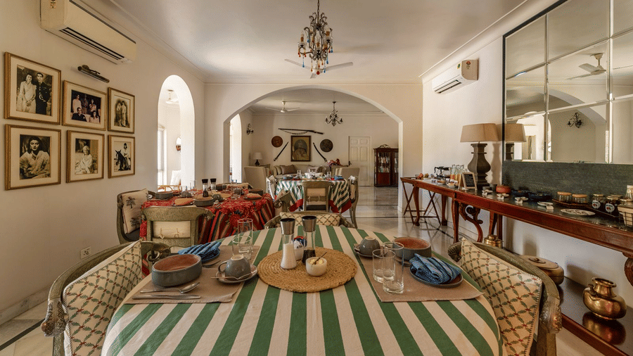 Dining room with a green and white striped tablecloth, a gallery wall of framed photos, a vaulted ceiling, and a large mirror at Barwara Kothi, Jaipur.