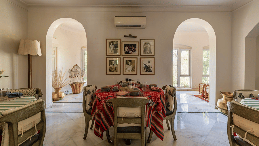 Dining room with a red and green striped tablecloth, framed photographs on the walls, and arched doorways at Barwara Kothi, Jaipur.