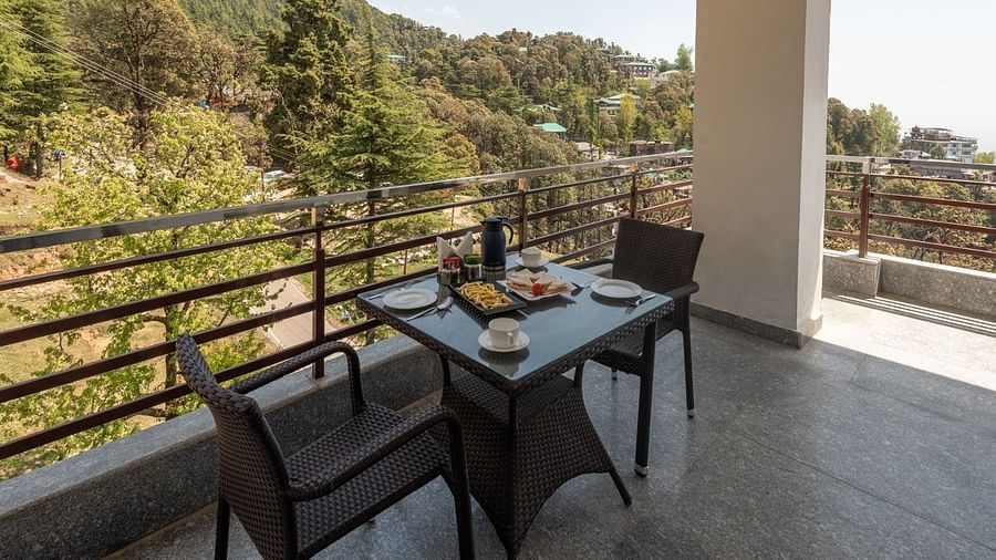 Balcony of Family Suite features an intimate seating table for two, spacious area and a view of the lush green hills and landscapes on a sunny day at DLS Hotel Shiva Sanctuary & Spa, Dharamshala.