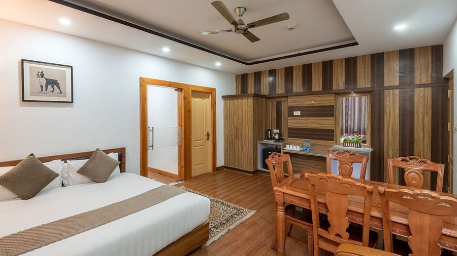 Double bed in the Family Suite of DLS Hotel Shiva Sanctuary & Spa, Dharamshala also furnished with a four-seating dining table and a shelf showcasing a minibar and coffee station.