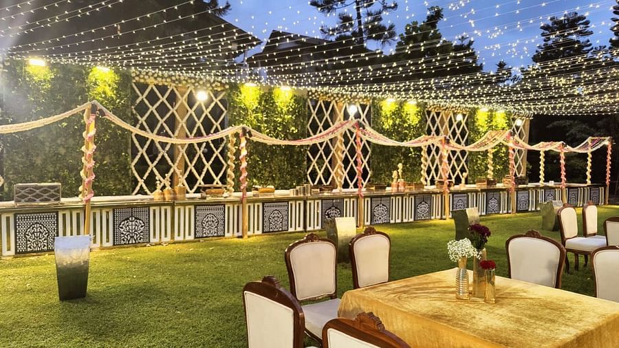 An outdoor dining area with tables, chairs, and a buffet table decorated with lights and greenery.