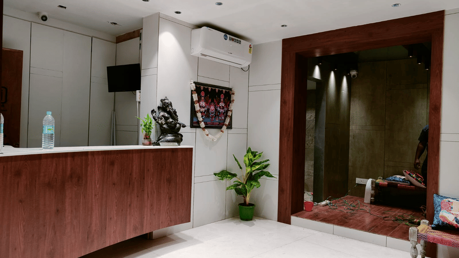 The hotel reception desk area with a dark wood counter, white walls, and a plant in the corner - Hotel Dolphin Puri
