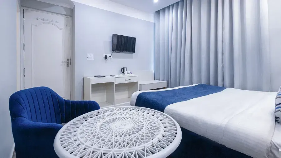 Deluxe Room featuring a king size bed with a white and blue cover, a round patterned side table, and a blue chair. - Hotel Downtown17, Chandigarh