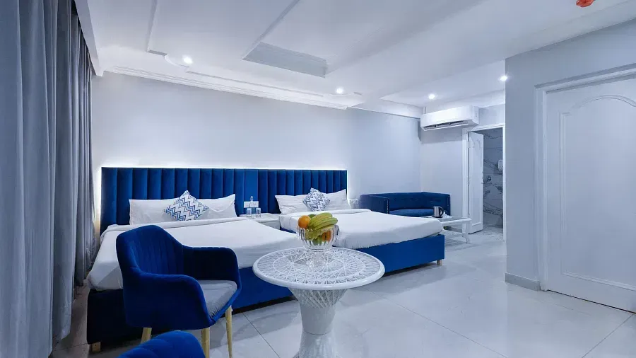 Family Room featuring blue-accented large beds, a white table with a fruit plate, and a clean, modern interior. - Hotel Downtown17, Chandigarh