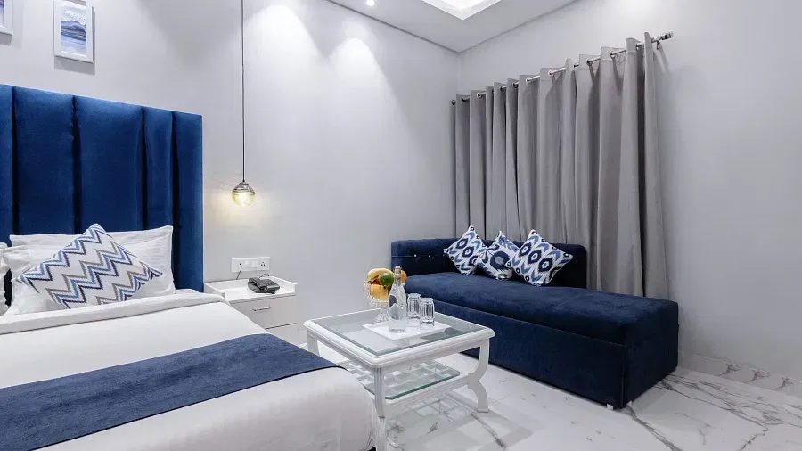 Super Deluxe Room featuring a blue cushioned bench, a glass-topped table, and neutral-toned curtains. - Hotel Downtown17, Chandigarh
